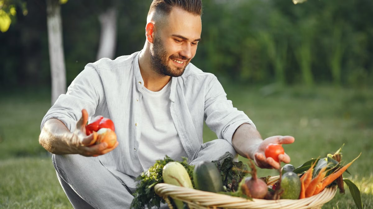Man seated outdoors with a basket of fresh vegetables, enjoying the garden.