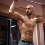 A bald, muscular man performing exercise on gym equipment indoors.