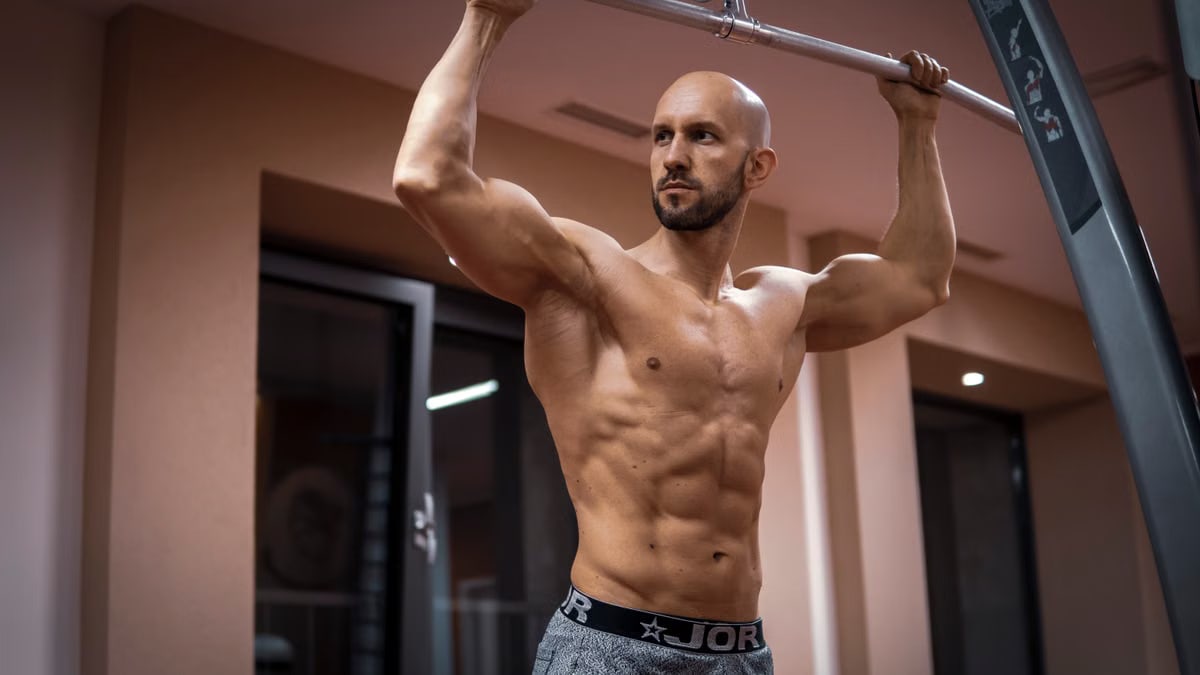 A bald, muscular man performing exercise on gym equipment indoors.